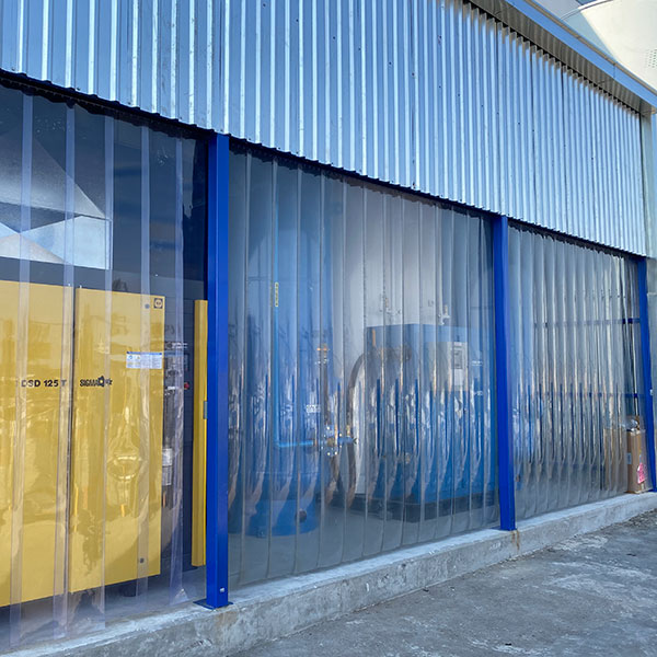 On-site PSA nitrogen generator installation with industrial compressor and buffer storage tanks behind PVC strip curtains in a protected outdoor enclosure.