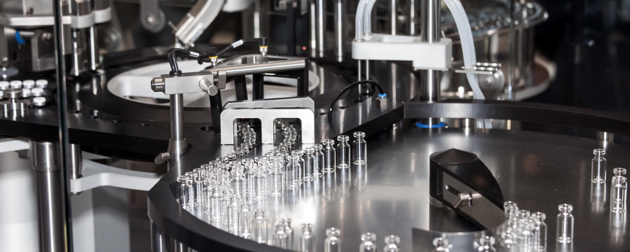 Automated rotary ampoule filling and sealing machine with rows of glass ampoules on a pharmaceutical sterile manufacturing line.